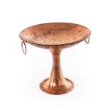 A large hammered copper pedestal bowl with two ring handles,