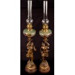 A pair of figural spelter oil lamps, with coloured glass reservoirs and clear glass chimneys,