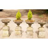 A set of four composition stone urns, each on a square plinth with wreath decoration,