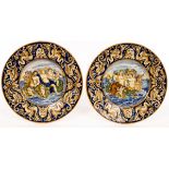 A pair of 19th Century majolica chargers painted allegorical scenes within a mask head and acanthus