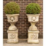 A pair of composition stone urns with lion mask ring handles and on square plinths with laurel