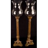 A pair of patinated metal candle holders of reeded column form with glass shades,