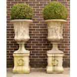 A pair of composition stone urns the sides decorated with Classical scenes,