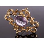 A Victorian brooch centred by an oval amethyst within a scrolling yellow metal frame,