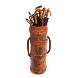 A leather shell carrier, now used as an umbrella stand, together with a quantity of shooting sticks,