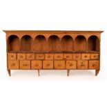 A pine spice rack with a seven-arch top, recesses over and fitted eighteen drawers,