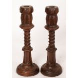 A pair of turned oak candlesticks with leaf and spiral design to the column,
