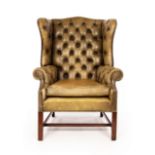 A wingback armchair upholstered in green leather with deep button back and arms,