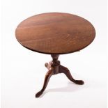 A circular oak tilt-top table, on a turned column and tripod support,