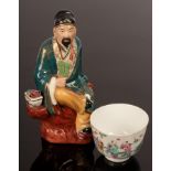 A 19th/20th Century Chinese porcelain figure of a scholar seated on a stone bench beside a pot of