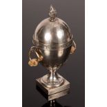 A silver coloured metal egg-shaped urn with flame finial to the cover, set on a pedestal base,