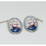 A pair of silver cufflinks with enamel panels depicting ships at sail.