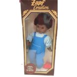 Zapf Creation boxed black vinyl doll wearing blue dungarees and gingham blouse. Excellent condition.