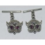 A pair of silver owl shaped cuff links with ruby eyes.