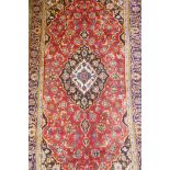 A vintage red ground fine woven Persian Kashan carpet with traditional floral medallion design,