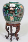 A Chinese famille noir jar with dragon decoration and six character mark to base, on a carved wood