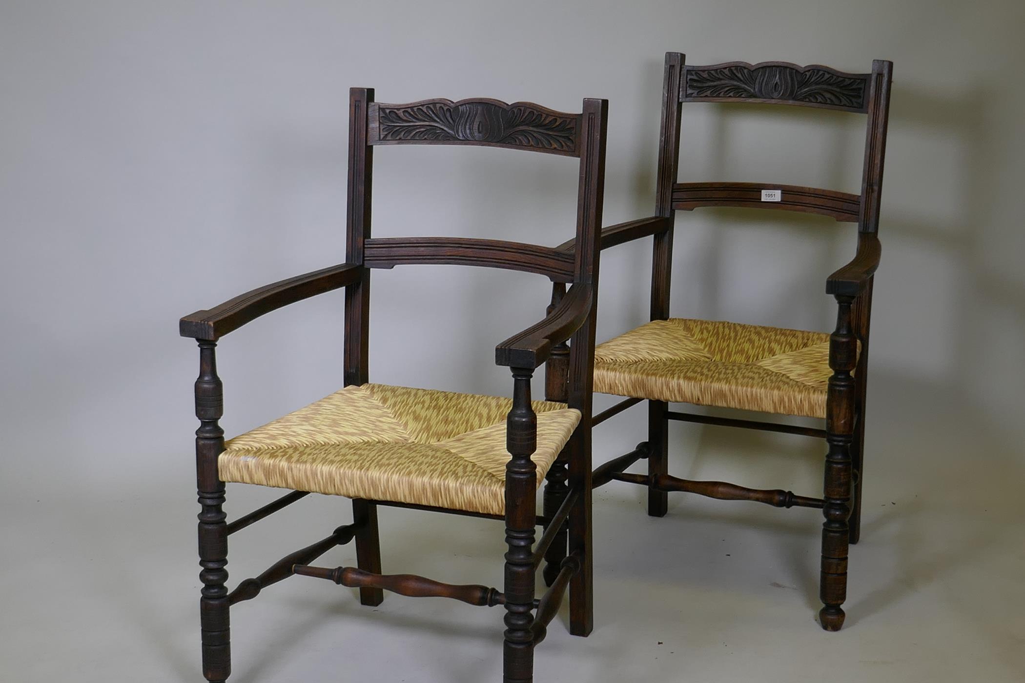 A pair of oak elbow chairs with carved back rails and rush seats, raised on turned supports