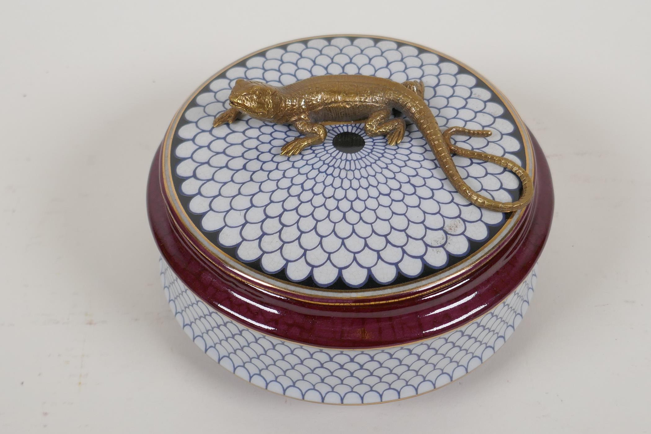 A porcelain trinket box, the cover with a bronzed figure of a lizard, 5½" diameter