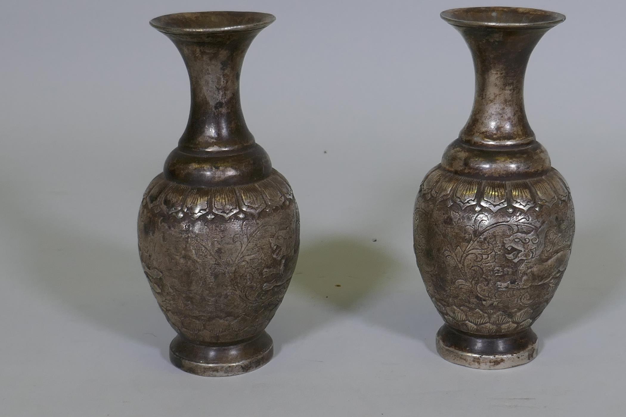 A pair of Chinese white metal vases with raised decoration depicting a lion chasing a deer, seal