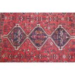 An Iranian red ground wool rug with three blue medallions and a geometric animal pattern, worn and