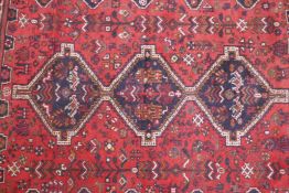 An Iranian red ground wool rug with three blue medallions and a geometric animal pattern, worn and