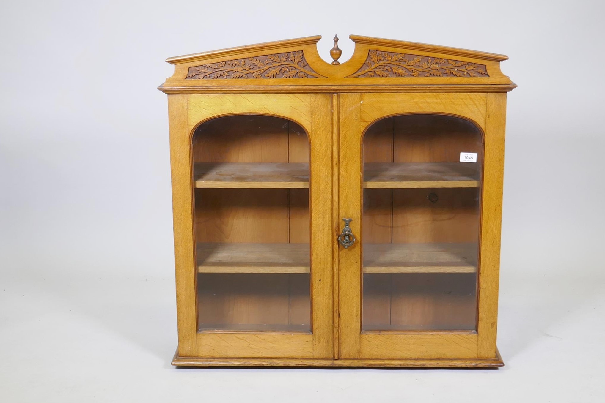 A Victorian golden oak cabinet, with carved oak and acorn pediment and two arched glazed doors,