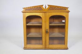 A Victorian golden oak cabinet, with carved oak and acorn pediment and two arched glazed doors,