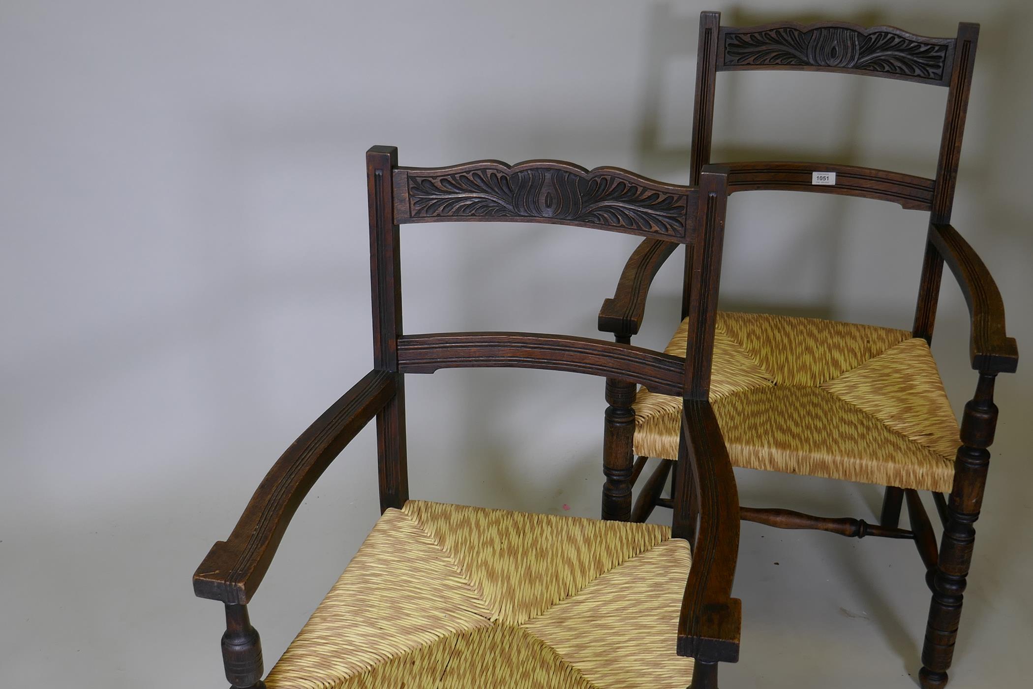 A pair of oak elbow chairs with carved back rails and rush seats, raised on turned supports - Image 2 of 2