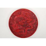 A Chinese cinnabar lacquer style dish with raised twin dragon and flaming pearl decoration,