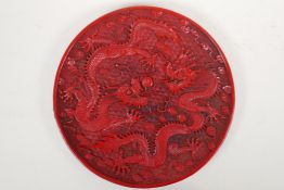 A Chinese cinnabar lacquer style dish with raised twin dragon and flaming pearl decoration,