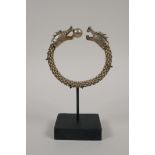 A Chinese white metal rope twist bangle with twin dragon head decoration to ends, on a display