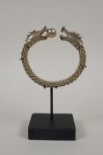 A Chinese white metal rope twist bangle with twin dragon head decoration to ends, on a display