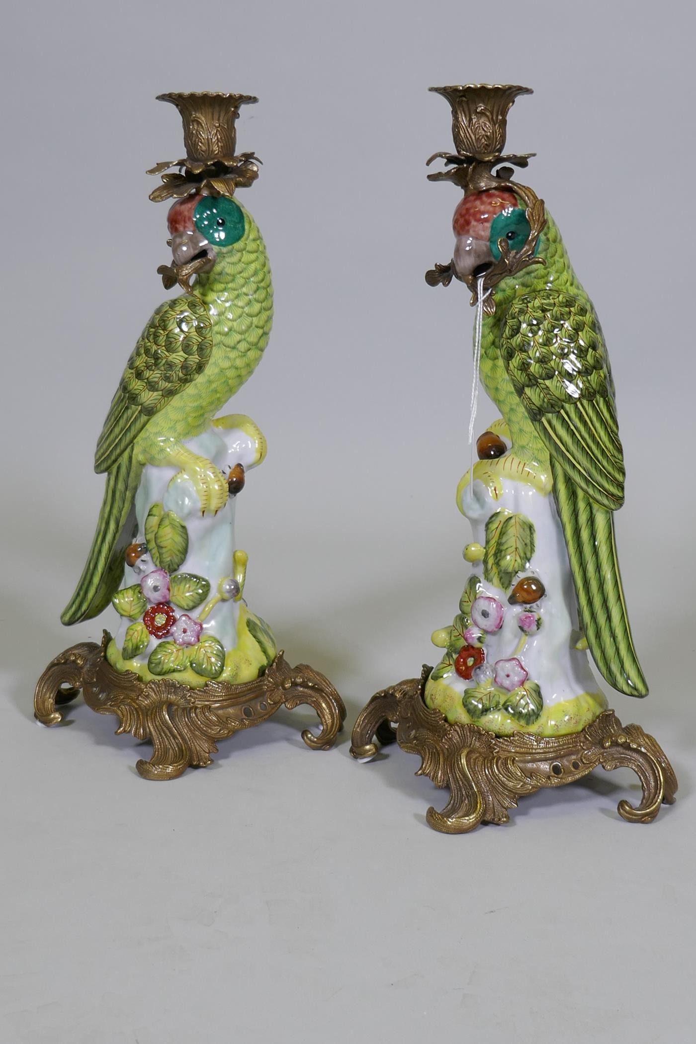 A pair of porcelain parrot candlesticks with brass mounts, decorated in bright enamels, marked to