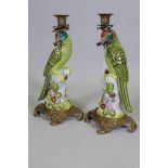 A pair of porcelain parrot candlesticks with brass mounts, decorated in bright enamels, marked to