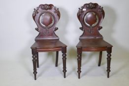 A pair of C19th mahogany hall chairs with carved crest shaped backs and bow front seats, raised on