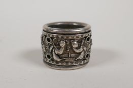 A Chinese white metal archers thumb ring decorated with figures on a revolving cuff, impressed