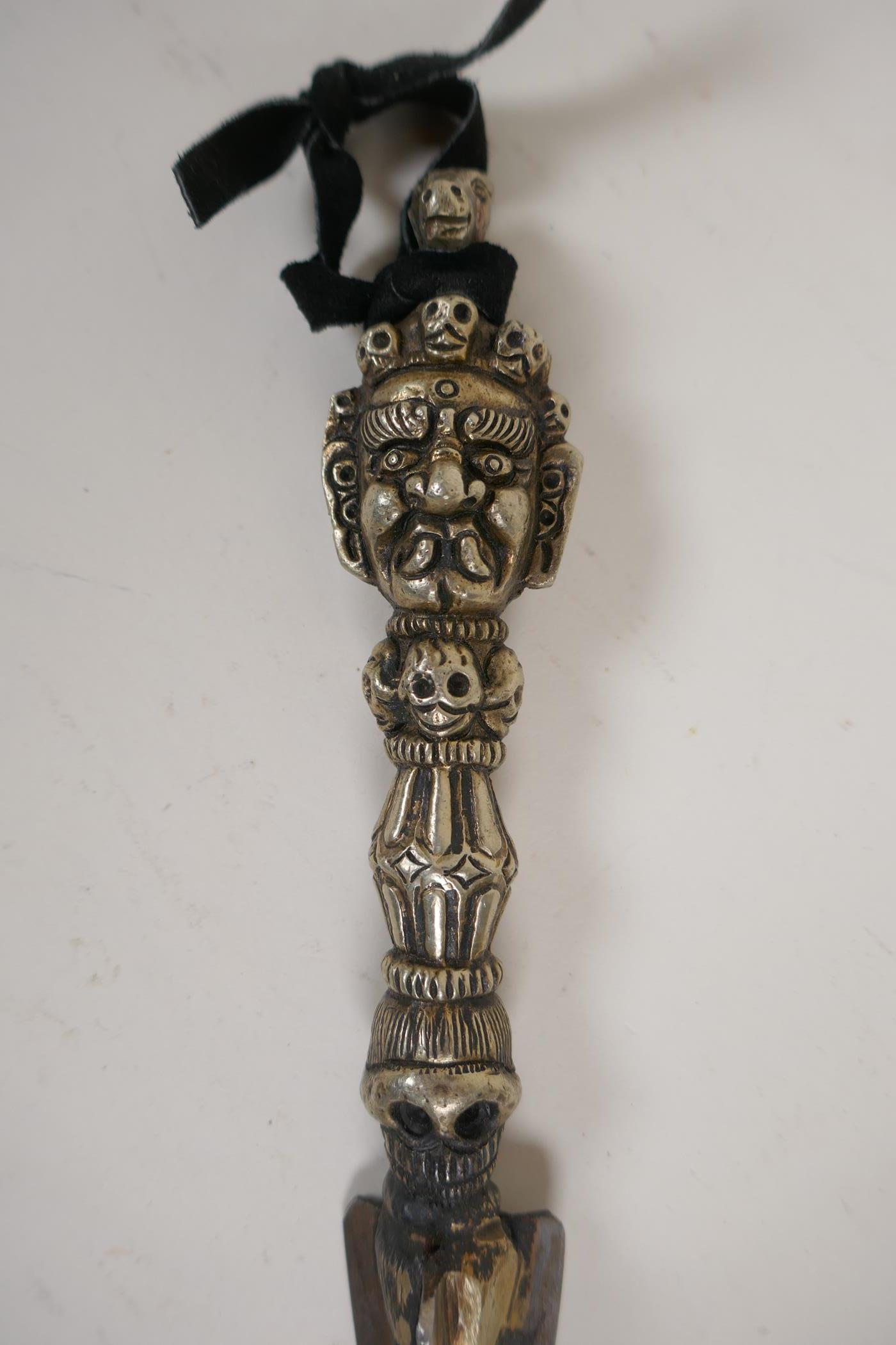 A Tibetan white metal phurba, the handle decorated with a wrathful deity mask and skulls, 9" long - Image 2 of 3