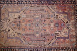 A Persian faded red ground wool rug with floral medallion design and blue borders, 90" x 57"