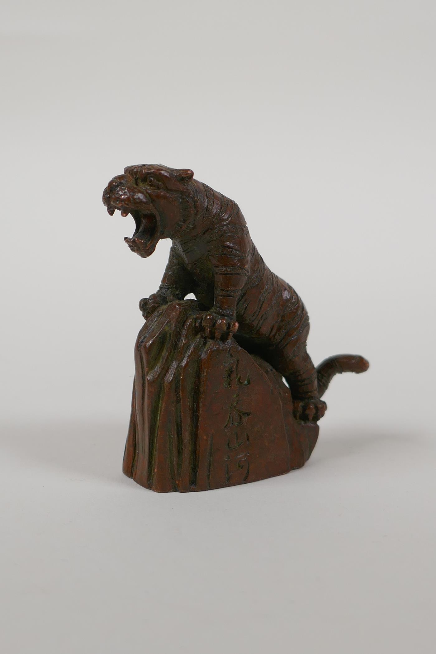 A Japanese bronze okimono of a tiger on a rock, character script to side, 2½" high