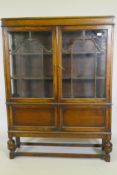 An Edwardian Jacobean style oak display cabinet with two glazed doors over two cupboards, raised