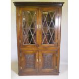 An antique oak corner cabinet with two glazed doors over two doors with carved panels, adapted,