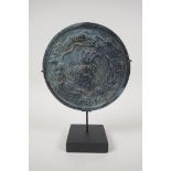 A Chinese bronze archaic style mirror with raised decoration of mythical creatures, on a display