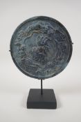 A Chinese bronze archaic style mirror with raised decoration of mythical creatures, on a display