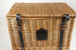 A wicker hamper with leather straps and handles, bearing a label for Harrods, London, 15" x 22" x