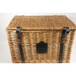 A wicker hamper with leather straps and handles, bearing a label for Harrods, London, 15" x 22" x