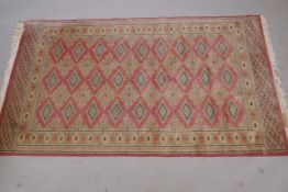 A tribal rug with geometric motifs on pink ground within three borders, 64" x 36"