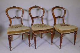 Three Victorian walnut balloon back chairs with carved crests, raised on tapering fluted supports