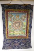 A Tibetan tangka, hand painted with gilt details, in an embroidered silk surround, 25½" x 33"