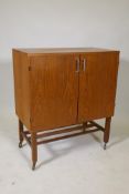 A mid century teak two door media cabinet, with fitted interior, raised on square supports with