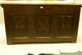 An C18th oak coffer with plank top and carved triple panel front, raised on stile supports